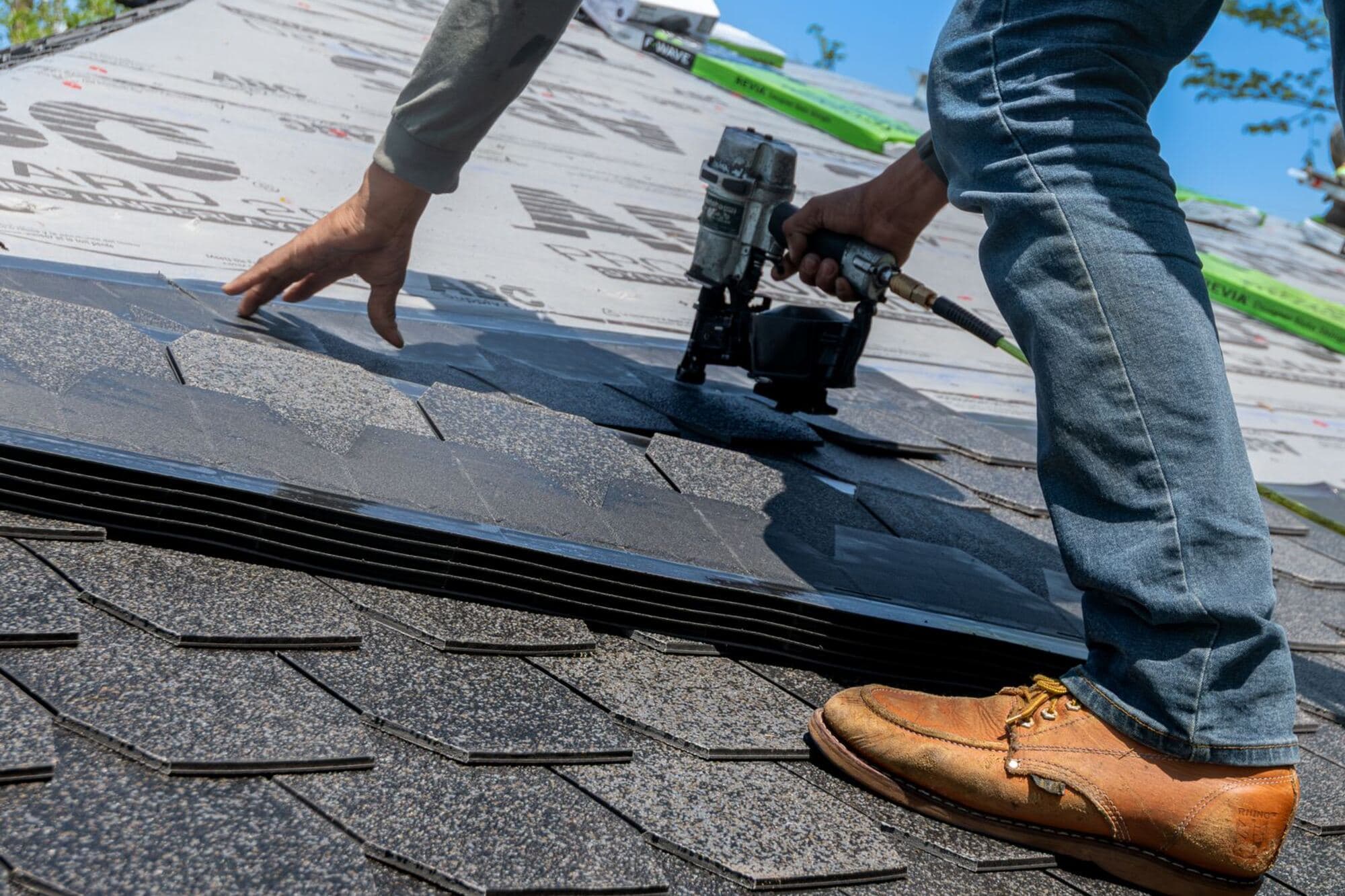Roofer fastening asphalt shingles with a nail gun
