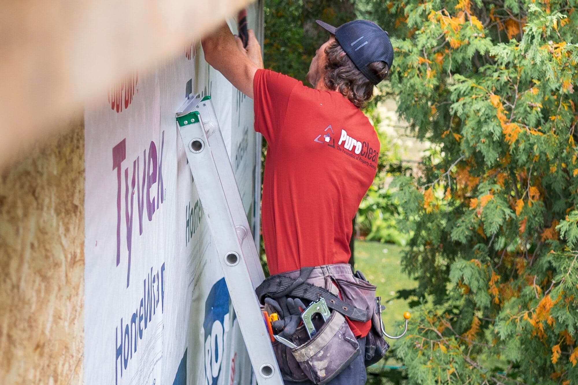 Worker on a ladder fastening house wrap before siding goes on